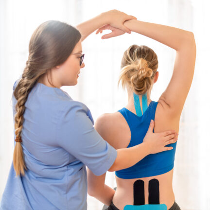 Young female patient wearing kinesio tape on her back and neck exercising with a professional physical therapist. Kinesiology, physical therapy, rehabilitation concept.